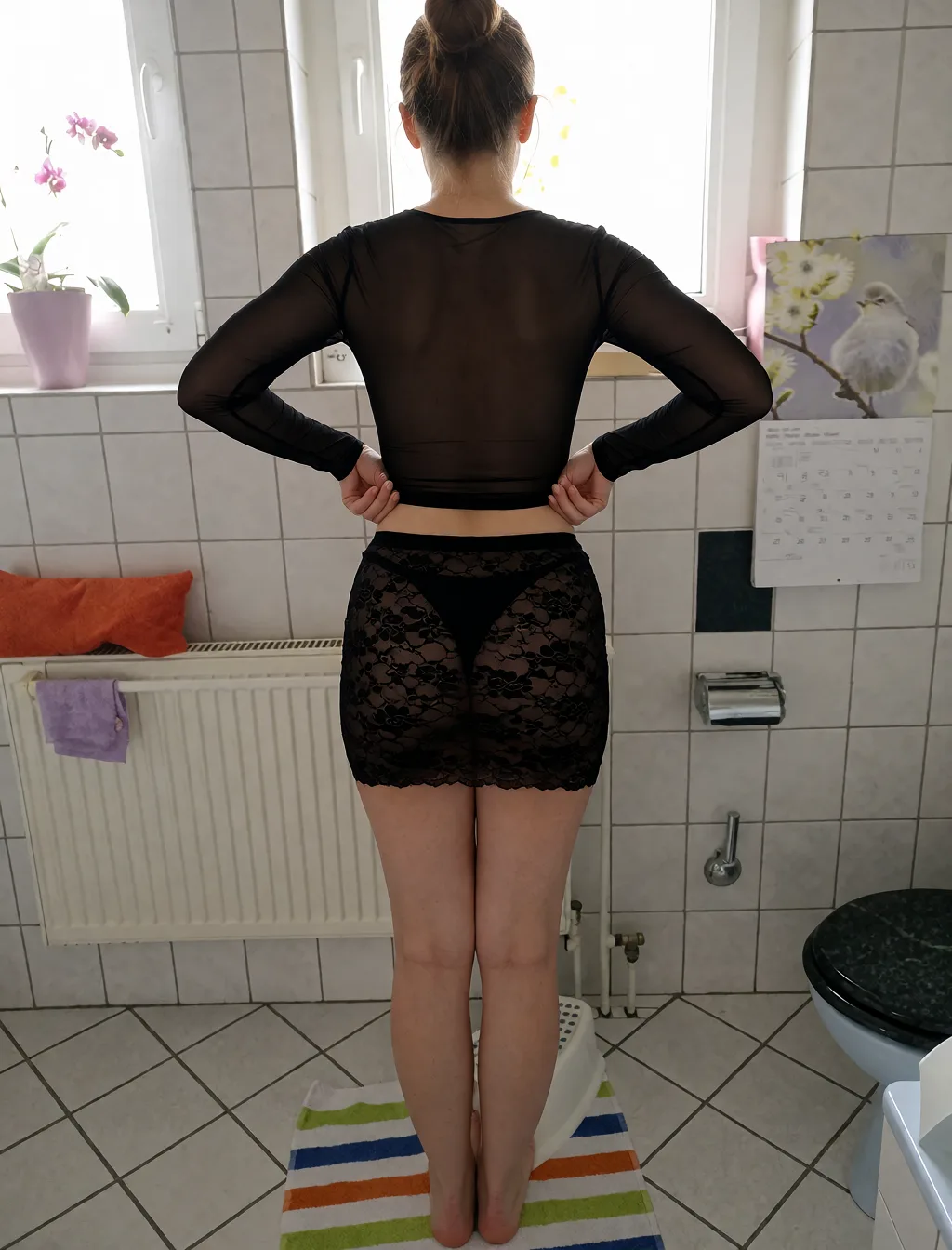 Edit the supplied photograph. Change only what is asked for below. Return one clean, natural, high-resolution photograph with realistic skin texture and no distortion. Slim her waist so the figure reads as an hourglass, keeping the shoulders and the hips as they are. Replace her outfit with a sheer black mesh top and a matching fitted skirt. Keep her face, her identity, her hair and her skin tone exactly as they are, and keep the room and the light she is in. Keep her pose and the framing of the shot.