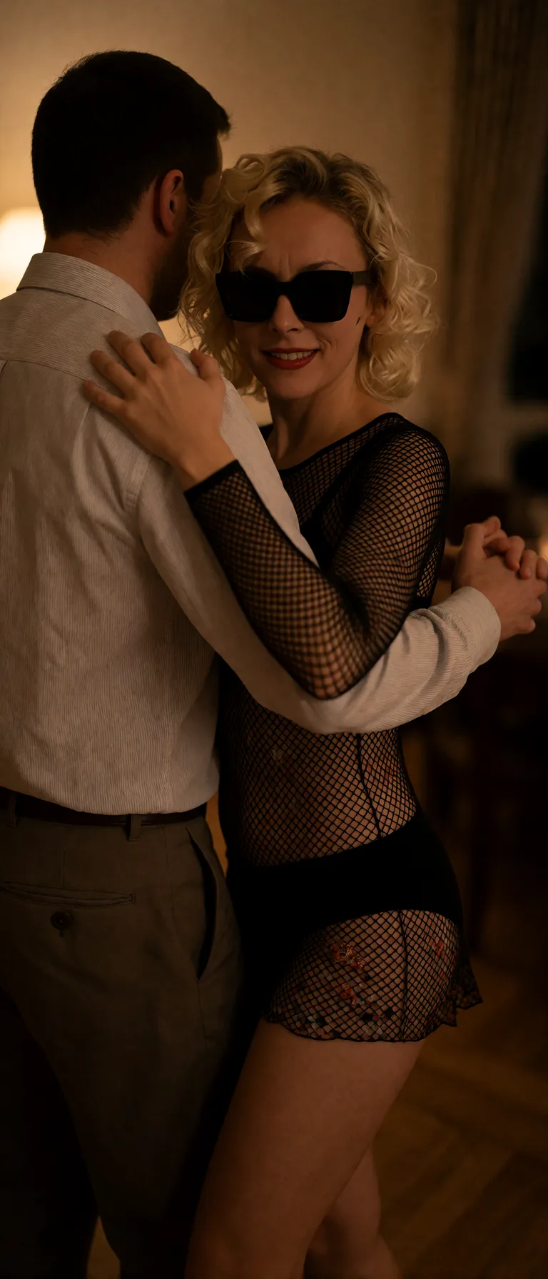 Edit the supplied photograph. Change only what is asked for below. Return one clean, natural, high-resolution photograph with realistic skin texture and no distortion. Replace her outfit with a black fishnet bodysuit worn over a plain black bra and briefs. Show her slow dancing with a partner in dim warm light, one hand on the partner's shoulder and the other held, looking towards the camera over the partner's arm; the partner wears an ordinary shirt and trousers. Keep her face, her identity, her hair and her skin tone exactly as they are, and keep the room and the light she is in.