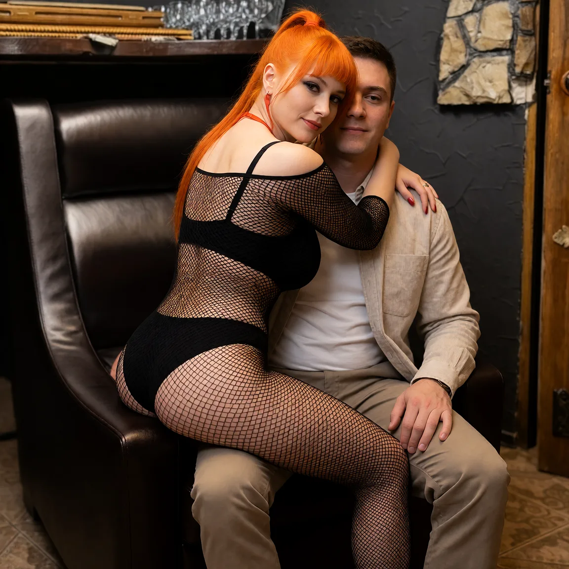 Edit the supplied photograph. Change only what is asked for below. Return one clean, natural, high-resolution photograph with realistic skin texture and no distortion. Make her chest noticeably larger and fuller, in a natural shape that suits her build, and let whatever she is wearing fall over it correctly. Replace her outfit with a black fishnet bodysuit worn over a plain black bra and briefs. Seat her sideways across a partner's lap with one arm around their neck, looking back over her shoulder towards the camera; the partner wears an ordinary shirt and trousers. Keep her face, her identity, her hair and her skin tone exactly as they are, and keep the room and the light she is in.