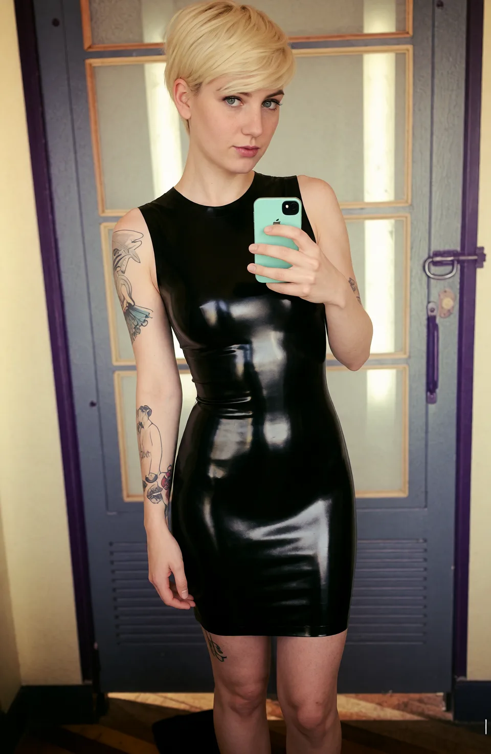Edit the supplied photograph. Change only what is asked for below. Return one clean, natural, high-resolution photograph with realistic skin texture and no distortion. Replace her outfit with a glossy black latex dress that fits closely, with realistic highlights on the material. Keep her face, her identity, her hair and her skin tone exactly as they are, and keep the room and the light she is in. Keep her pose and the framing of the shot.