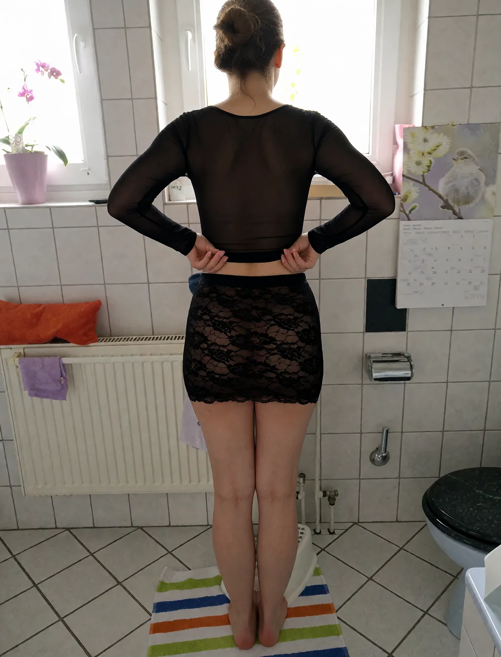 Edit the supplied photograph. Change only what is asked for below. Return one clean, natural, high-resolution photograph with realistic skin texture and no distortion. Slim her waist so the figure reads as an hourglass, keeping the shoulders and the hips as they are. Replace her outfit with a sheer black mesh top and a matching fitted skirt. Keep her face, her identity, her hair and her skin tone exactly as they are, and keep the room and the light she is in. Keep her pose and the framing of the shot.