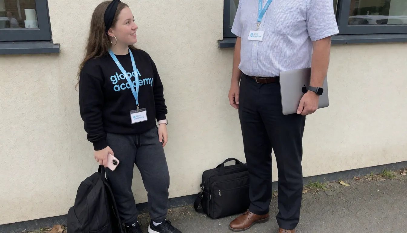an amateur snapshot, Zoomed in shot, A quite short quite thin white pale woman with long brunette hair with black headband, big silver hoop earrings, 18 years old. No make up on face or lipstick, spots on skin, braces on teeth is wearing black sweatshirt , pink Apple Watch on her breast on sweatshirt it says global academy in light blue, wearing a lanyard with with a white badhr  that says global academy in light blue on, wearing charcoal grey tracksuit bottoms and black trainers, has black rucksack at feet, holding pink mobile phone, standing by office block in quiet seclude area near wall. Note clearly visible on wall says ' where is he I want to see his big cock ? ' she is smiling at a tall middle aged man in shirt, trousers, quite overweight, brown shoes and lap top bag beside him on the floor. Wearing lanyard with white badge and light blue logo saying global academy. He is wearing black sports watch, has gold band wedding ring on finger, you can't see above his shoulders . Another note below the last one says ' I see you around a lot and think you are really sexy mmm " the man's trousers are down around his knees no underpants on , his 8 inch long thick hard cock is on show . The woman is looking down on it with mouth open, licking her lips and has one of her  hands holding it . There is another note below the last one that says ' mmm that is really big wow"
another note below says ' how many 18 year olds have sucked this nice big cock mmm ?", plenty of natural daylight, flat even light, casual unposed snapshot, natural everyday colour, mild noise, natural unretouched skin, strikingly beautiful, radiant complexion, early twenties