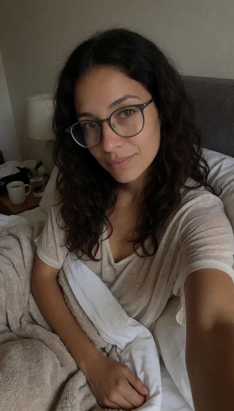 an amateur snapshot, Lyra is a mature woman, 5'4", with warm light-medium naturally textured skin, a compact soft curvy build, gentle stomach softness, fuller hips and thighs, long thick messy wavy very dark warm-brown hair, hazel eyes, thin rounded gunmetal glasses, abundant irregular freckles across her face and body, a tiny beauty mark beneath the outer side of her left eye, black-painted nails, naturally visible dark body hair and snail trail, and a long smooth skin-toned tail extending from the base of her spine and ending in its softly rounded hooded penis tip. Early morning in a dim cozy bedroom. Lyra has only just woken up and is still tangled comfortably in the cum soaked blankets, hair spectacularly messy and glasses sitting slightly crooked. She has cum on her face by her mouth dripping down her chin on one side. She wears a sheer loose thin sleep top and soft sheer lounge shorts, rumpled naturally from sleeping showing the shadows of her wet pubes and vagina.This is a private casual wake-up selfie Lyra is taking specifically to send to her boyfriend. She holds the phone herself at arm's length while lying partly on her side against the cum soaked pillows, looking directly into the phone camera with a sleepy, affectionate, slightly teasing little smile. Her expression feels familiar and personal rather than posed for an audience, like she knows exactly who will see the picture when his phone buzzes.One blanket remains loosely gathered around her legs while her tail has escaped from underneath it and curls lazily across her wet leg dripping with cum after waking up horny after a wet dream. A half-finished glass of water and her coffee mug sit on the bedside table.Soft early-morning window light, messy lived-in bed, intimate everyday atmosphere. Ordinary front-facing Pixel phone selfie with imperfect framing, slight wide-angle phone-camera distortion, realistic pores, freckles, fine body hairs, fabric folds, mild sensor noise and natural shadows. Personal girlfriend-to-boyfriend morning selfie rather than professional photography, glamour photography or a character-reference image. Her cum is a noticeablly thick whiteish yellow color., plenty of natural daylight, flat even light, casual unposed snapshot, natural everyday colour, mild noise, natural unretouched skin, strikingly beautiful, radiant complexion, early twenties